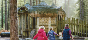 3 children running towards the House of Baba Yaga play structure in the forest