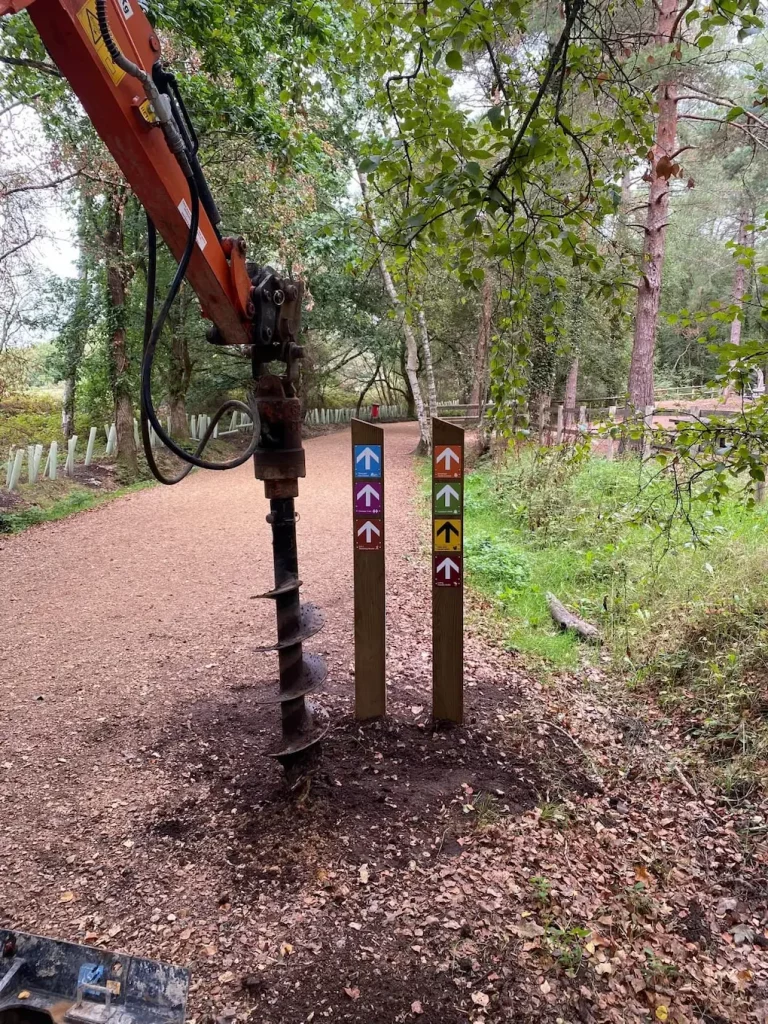 A construction drill next to two wooden posts with coloured arrows for trail directions on a forest path.