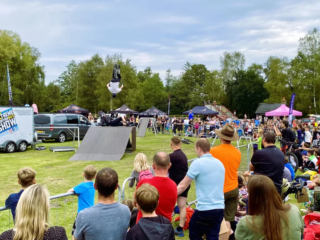 A crowd watches as a BMX rider performs a mid-air trick over ramps at Pedal at the Park Moors Valley.